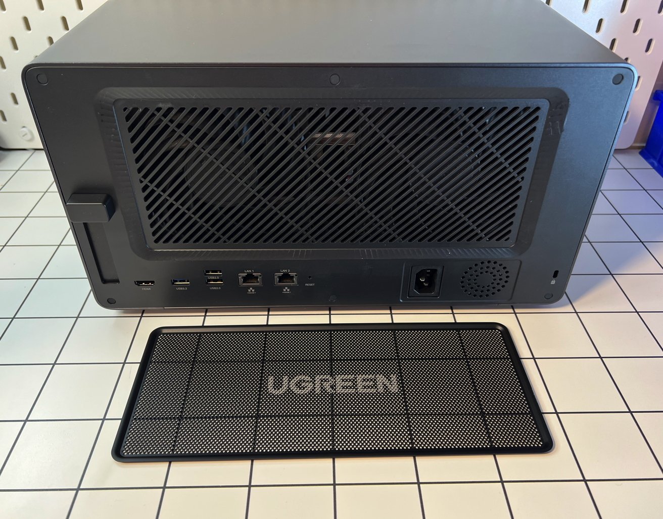 A black compact network attached storage device with visible ports and a brand-labeled grille on a tiled surface.