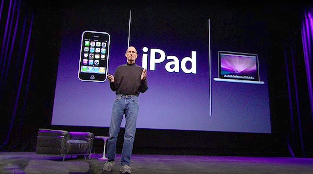 Person on stage presenting an iPhone, iPad, and MacBook Pro with a purple background.