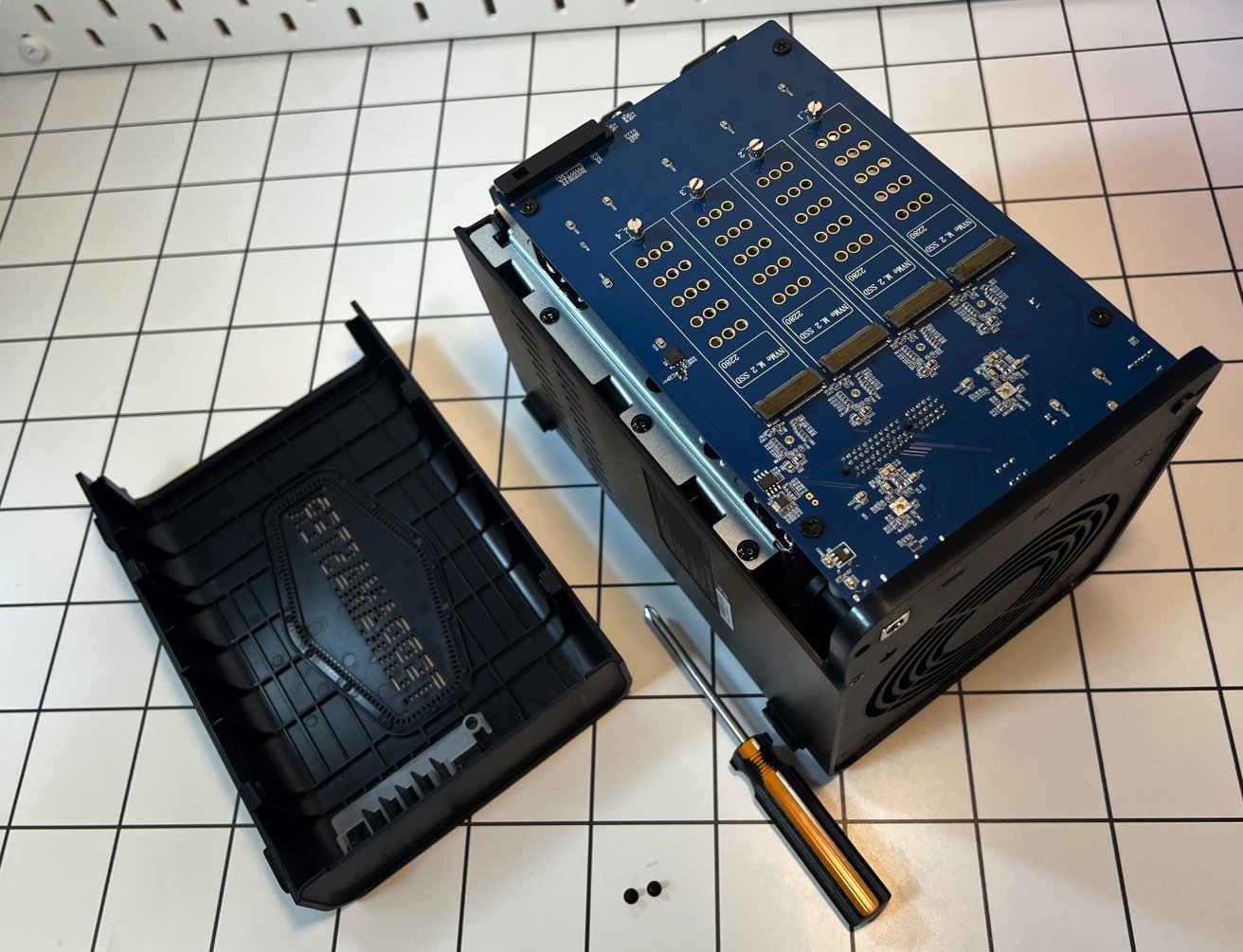 Open TerraMaaster D8 Hybrid with motherboard exposed, screwdriver, and screws placed on a white grid-patterned surface.