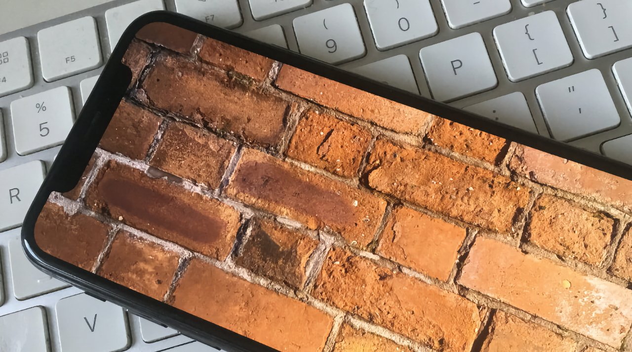 Smartphone displaying brick wall texture rests on a white computer keyboard.