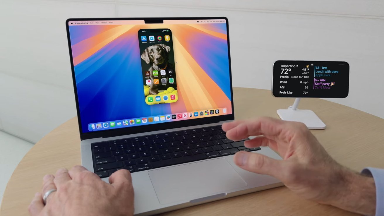 Person interacting with a laptop displaying a mirrored iPhone screen with a dog wallpaper. Weather and calendar info shown on a stand next to the laptop.