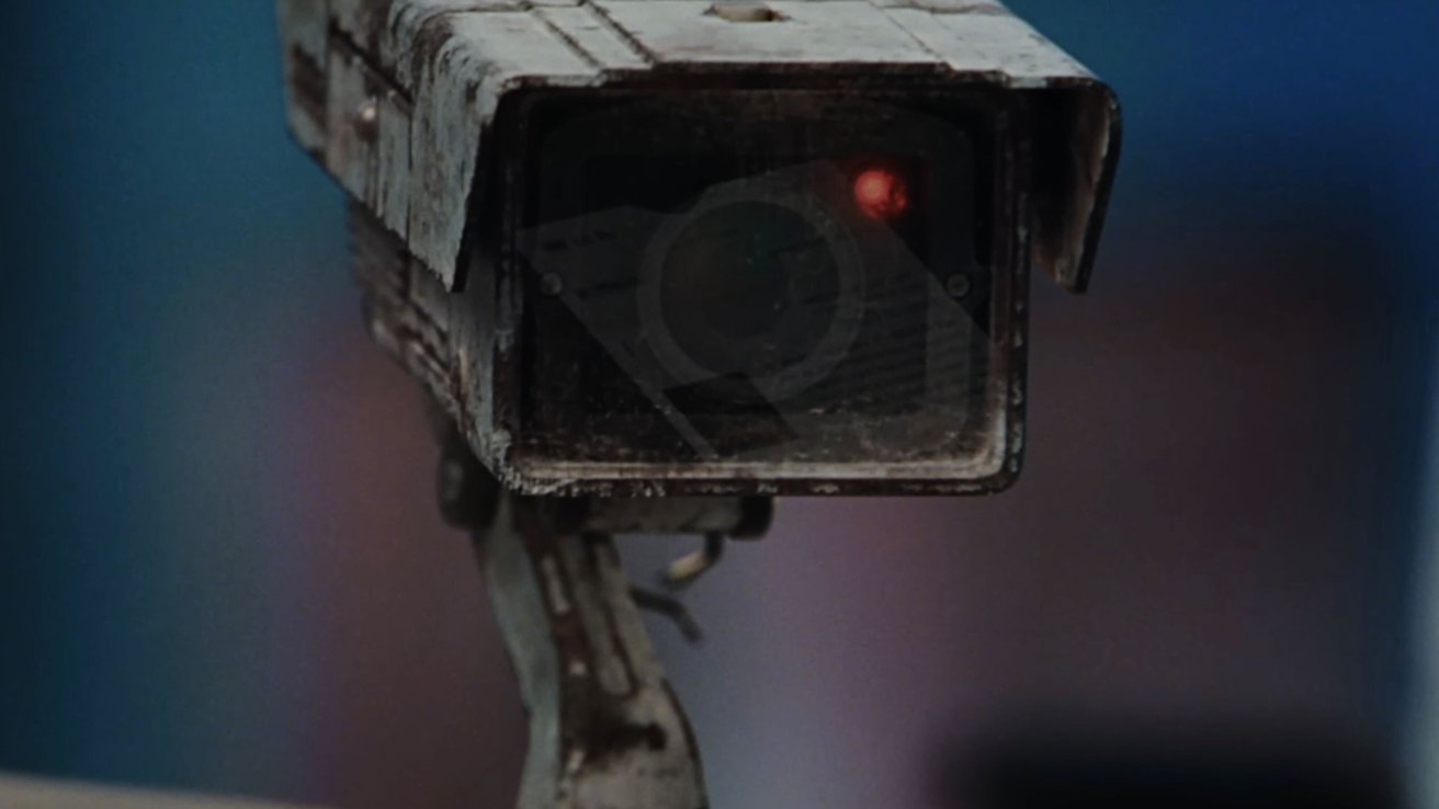 Close-up of a rusty, weathered security camera with a dark lens and glowing red light against a blurred background.