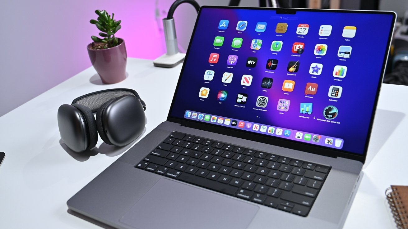 Laptop on a desk displaying app icons, next to over-ear headphones and a small potted plant.