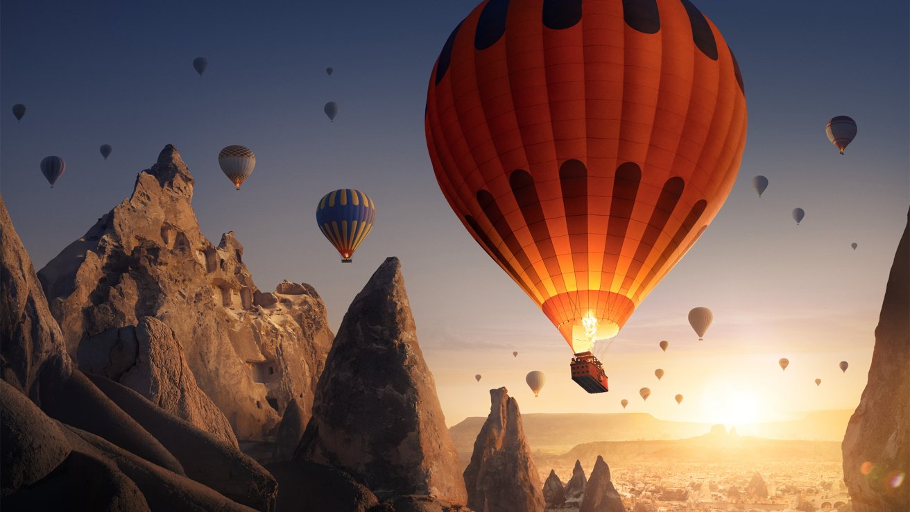 Hot air balloons soar above jagged rock formations at sunrise, creating a picturesque and serene scene. The sky is clear and the landscape glows in the soft morning light.