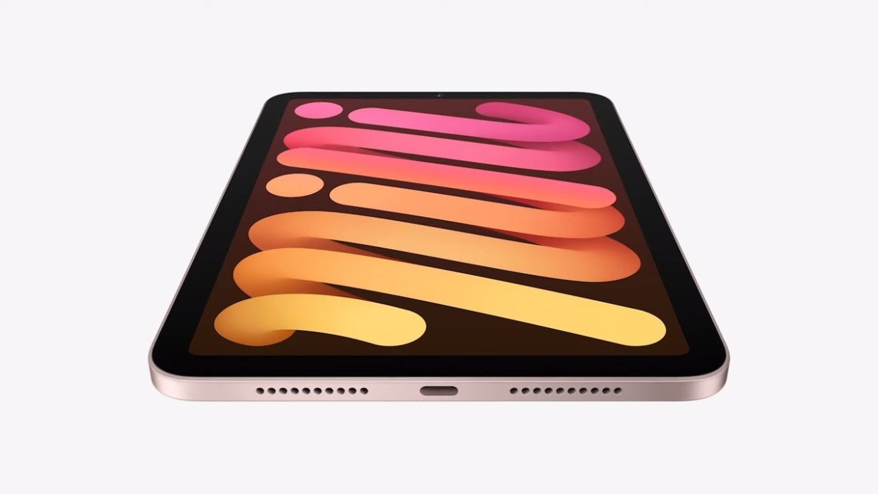 Tablet with a colorful abstract wallpaper featuring pink, orange, and yellow shapes, viewed from a low angle. The device has a slim profile and visible speakers.