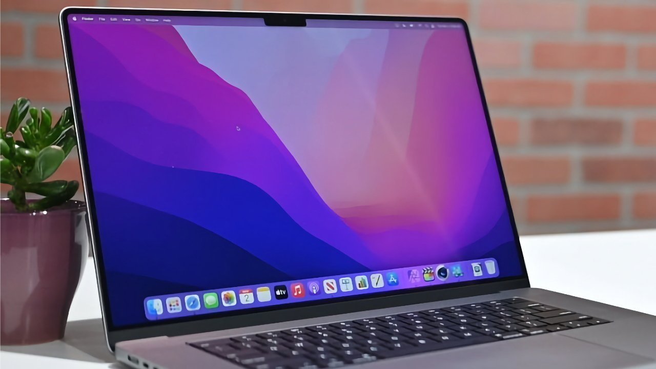 Laptop with a vibrant purple-pink screen on a desk beside a green potted plant, against a brick wall backdrop.