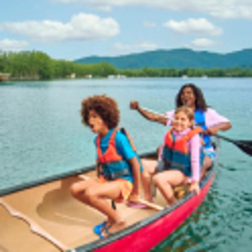 Duas crianças e um adulto riem enquanto atravessam um lago de canoa. 