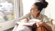 A young woman sitting on her couch and practicing a gratitude exercise by writing in her gratitude journal.