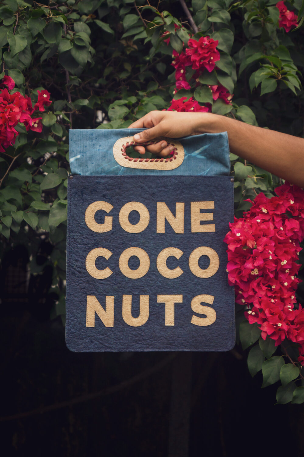 a bag made from coconut waste water is held up in front of bright pink flowers, vegan leather 