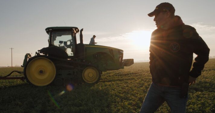 A man stands in a field next to a tractor