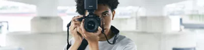 Image of a man holding a camera with flash in front of him with a cityscape in the background