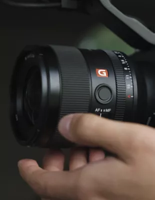 A hand adjusts a Sony G Master E-mount lens