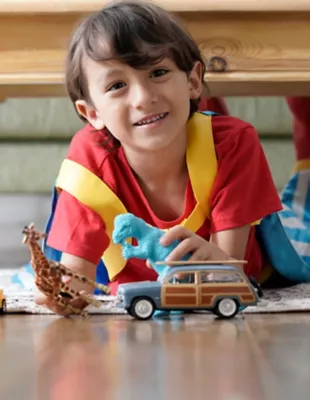 A boy wearing a red t-shirt plays with toys on the floor