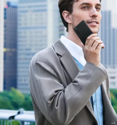 A man in a grey suit holds a black smartphone up to his cheek