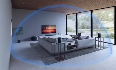 Grey sofa, table and chair in a living room with wall-mounted TV and soundbar on a plinth, and glass patio doors to the right overlooking a garden, with blue sphere highlighting surround sound