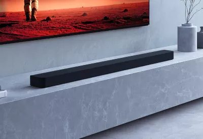 Barre de son BRAVIA Theatre Bar 9 sur un socle en marbre avec des objets de décoration à gauche et des vases à droite, ainsi qu'un téléviseur fixé au mur au-dessus montrant une personne dans un désert rouge