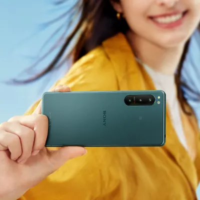 Woman in an orange jacket holding an Xperia 5 IV in front of her, with a blue sky behind