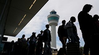 Reisende stehen vor dem Terminalgebäude des Amsterdamer Flughafens Schiphol an, um einzuchecken und an Bord zu gehen.