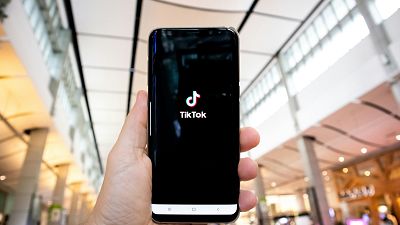 Una persona con in mano uno smartphone che mostra il logo dell'applicazione TikTok