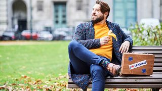 Jeune homme sur un banc avec une valise affichant le logo Erasmus (21/10/2019).