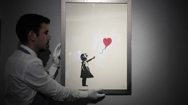 Un membro dello staff posa per una foto con una stampa di "Girl with Balloon, 2004" dello street artist britannico Banksy presso la casa d'aste Bonhams di Londra, 8 novembre 2021.