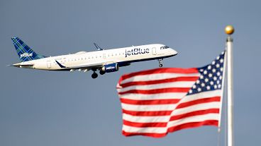 Um jato de passageiros da JetBlue passa junto à bandeira dos EUA.