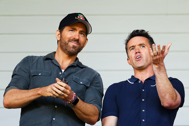 <p>Reynolds and McElhenney watch on at Wrexham’s Racecourse Ground</p>