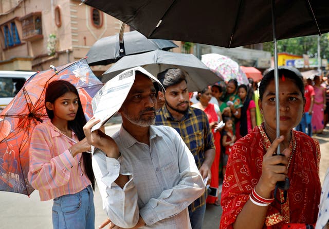 <p>People use umbrellas and newspapers to beat the heat as they wait to vote in West Bengal on 20 May 2024</p>