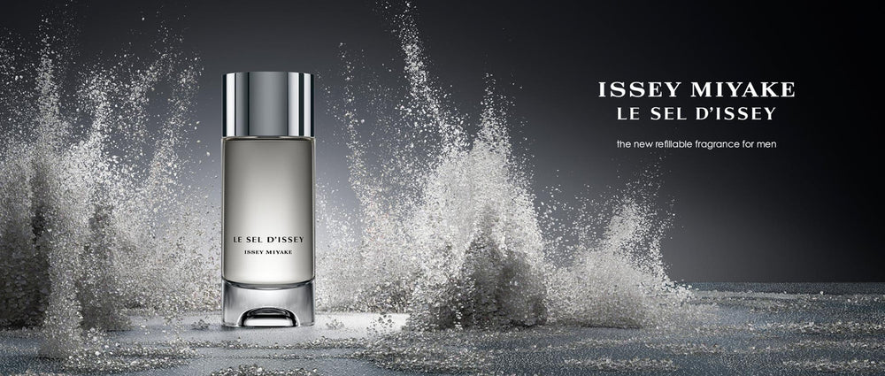 Cylindrical perfume bottle with silver cap stood on grey surface with grains of salt splashing around it. "ISSEY MIYAKE LE SEL D'ISSEY the new refillable fragrance for men" written in white.