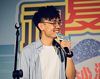 Terence Lam is holding a microphone that says "初秋樂 Band Fun" at the top and "屯門沙灘節2019" at the bottom.