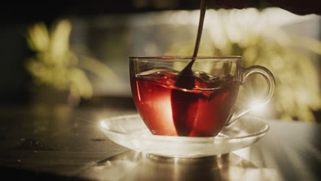 sugar is stirred in a glass cup of tea. the morning sun illuminates the hot drink beautifully