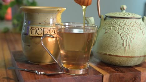 making herbal tea in a green teapot on a wood table in a light and airy room with green plants in the background and a glass teacup