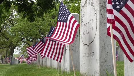 close up side view of gravestones in a cemetery of civil war soldiers remains on memorial day with american flags flapping in the wind