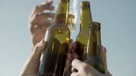 close up of unrecognizable friends raising and clinking bottles of beer