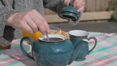 hand takes lid from teapot to stir at outdoor breakfast table, slow motion