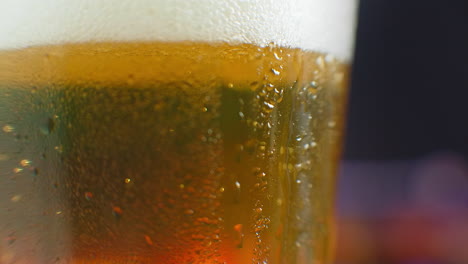 macro shot of a drop running over a glass of beer. sweat on a cold glass of beer. a dripping drop on a glass filled with beer.