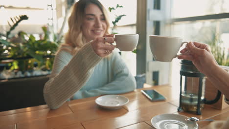 young female friends toasting with cups of tea and coffee