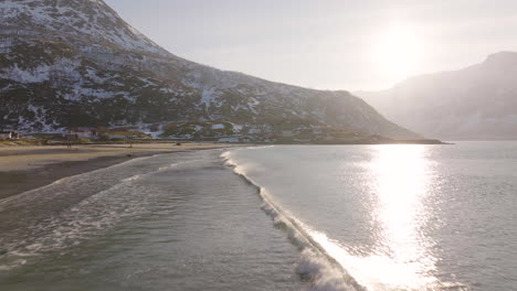 small waves run onto sandy arctic beach, patchy snow on mountain