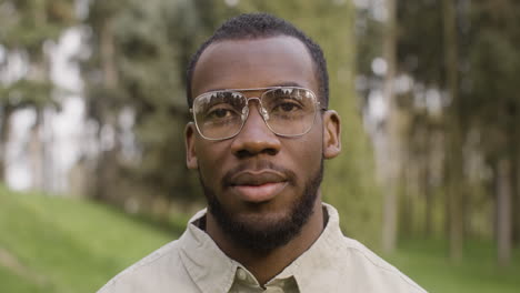 portrait of an american man with eyeglasses standing in the park looking at the camera and around