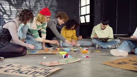 young environmental activists painting placards sitting on the floor