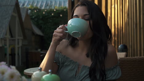 portrait of a young hispanic latina good looking woman drinking coffee or tea and smiling while sitting outdoor