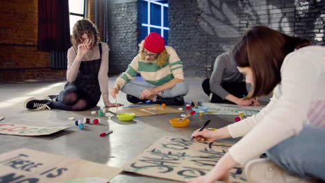 young environmental activists painting placards sitting on the floor