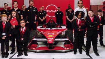 Nissan Formula E team members, and a group of children (the Department of Futures) in black suits standing in front of a red Nissan Formula E race car