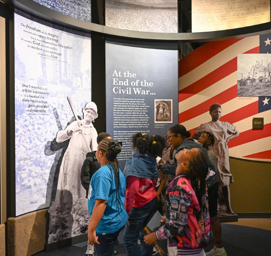 A group of children standing together, facing left, and looking up towards a Civil war museum exhibit.