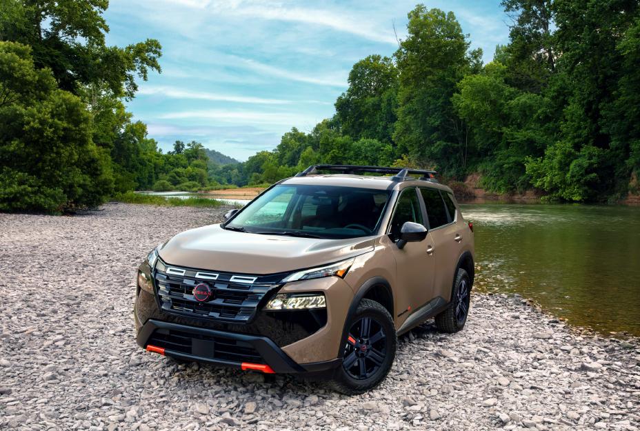 Front left 3/4 angle of the 2025 Nissan Rogue rock creek parked on rocks in front of a wooded creek.