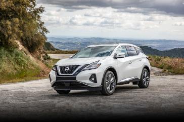 Front left ¾ angle of a white 2024 Nissan Murano parked on a mountain side road overlooking more mountains on a cloudy day