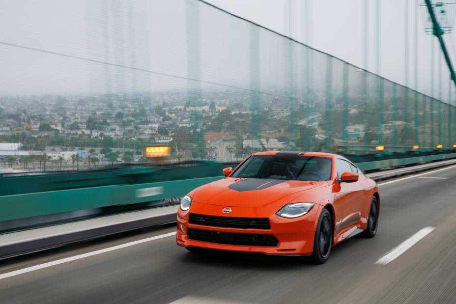 Orange Nissan Z Heritage Edition driving on a bridge with a city in the background