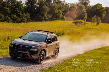 Raised front left ¾ angle of  a 2025 Nissan Rogue Rock Creek barreling over a dirt road with dust flying behind.