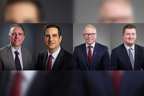 A collage a four executive headshots, all smiling and in dark suits, two were a red tie, one a black, and a one a plaid tie.