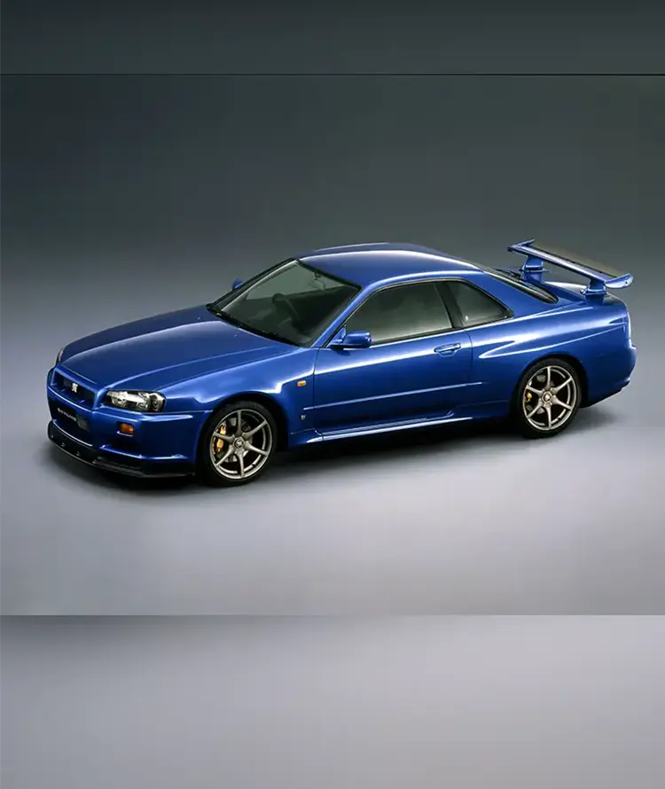 Front left 3/4 view of a blue 1999 Nissan GT-R on a plain gray backdrop.